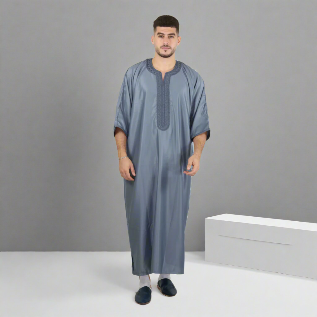 Man wearing a long gray dress with embroidery on a white background